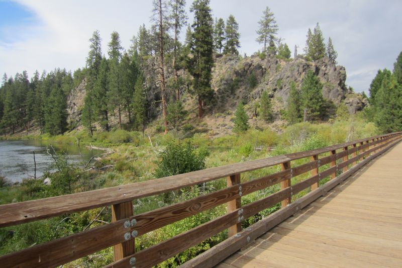 Wooden bridge over the Deschutes River on the trail to Benham Falls, with pines and a rocky bluff beyond