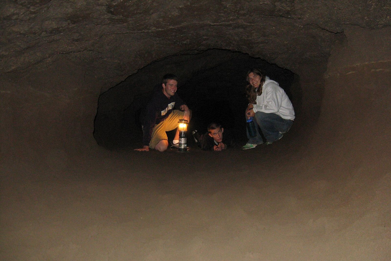 Visitors with a lantern resting in a low section of the Lava River Cave tube