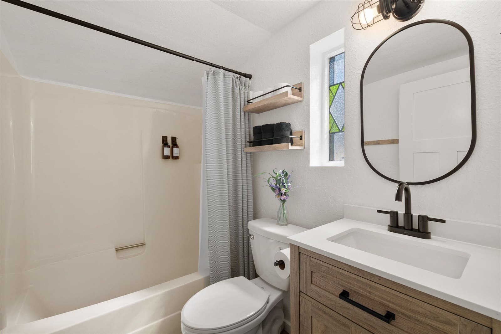 Full bathroom with a tub and shower, wood vanity, and arched mirror
