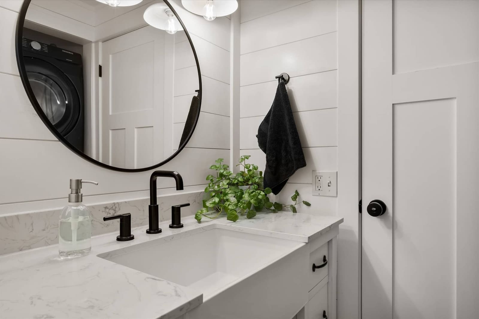 Bathroom vanity with a round mirror, black fixtures, and stone countertop
