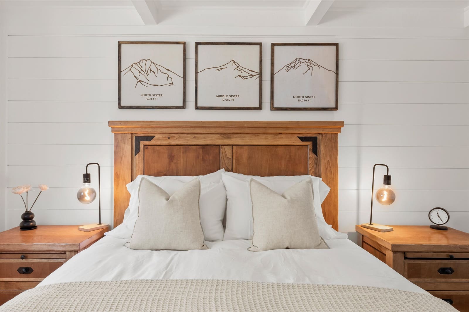 Bedroom one, a queen bed with a wood headboard and three framed mountain prints on the shiplap wall