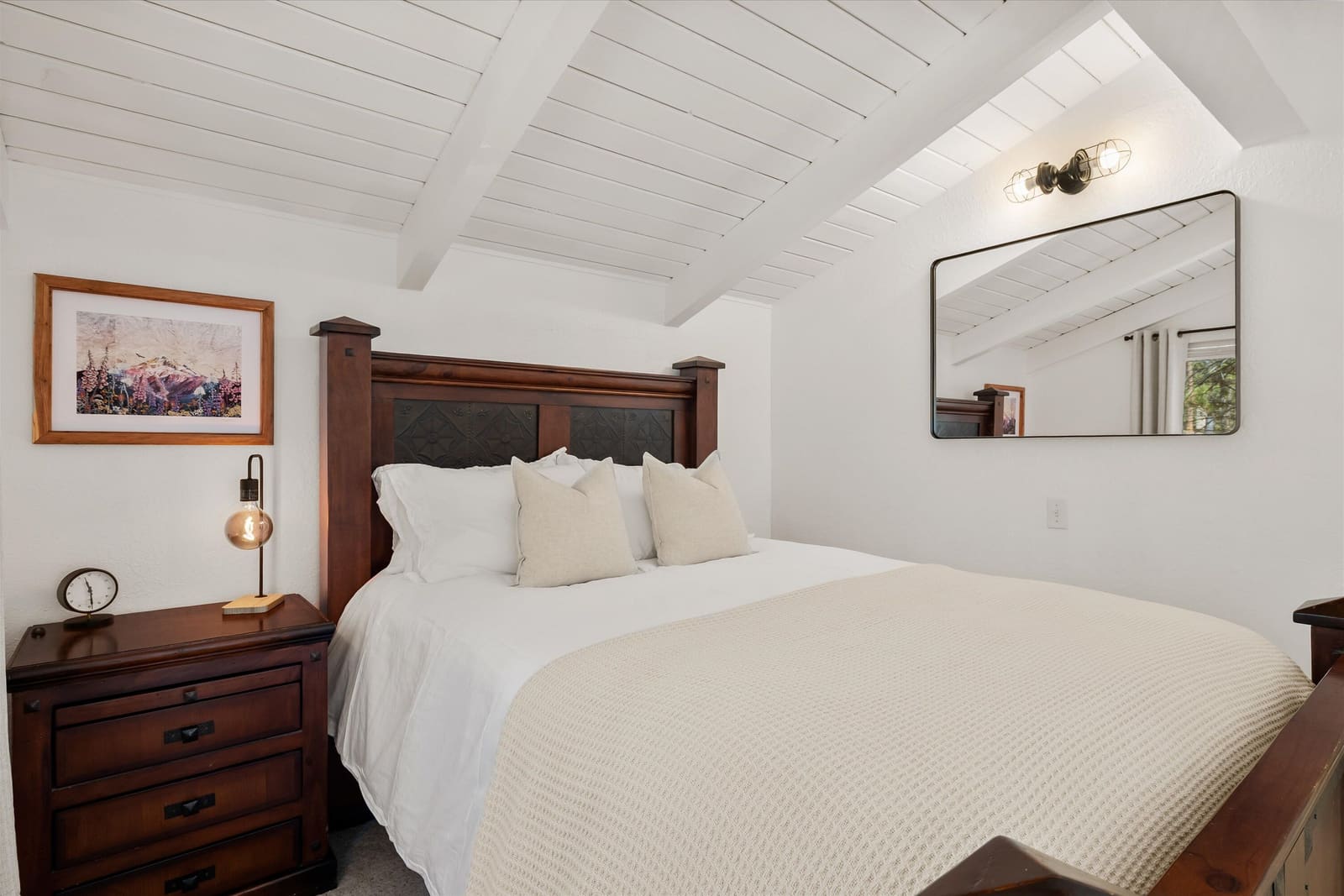 Bedroom two, a queen bed with a dark carved headboard under the vaulted plank ceiling